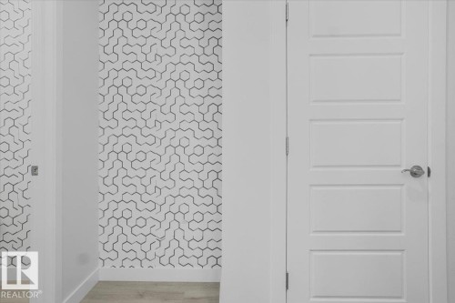 Contemporary interior hallway featuring a honeycomb pattern accent wall, white trim, and a five-panel interior door with brushed nickel hardware - 2852 Duke Crescent, Edmonton, AB 