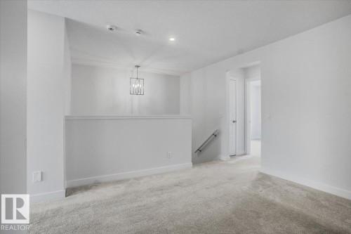 Carpeted loft area featuring a contemporary chandelier, recessed ceiling lighting, textured ceilings, white baseboards, and a metal handrail - 2852 Duke Crescent, Edmonton, AB 