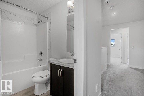 Bathroom featuring a white tub and shower combination with a decorative tile surround, a dark wood-finish vanity with a white countertop and undermount sink, and wood-finish flooring - 2852 Duke Crescent, Edmonton, AB 