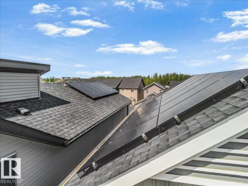 Roofline featuring multiple solar panel installations, asphalt shingles, and light-colored siding - 2852 Duke Crescent, Edmonton, AB 