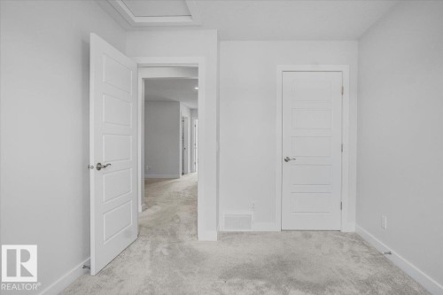 Interior room featuring light gray wall paint, light gray carpeting, and multiple white paneled doors with brushed nickel hardware - 2852 Duke Crescent, Edmonton, AB 