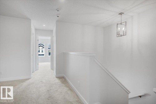 Upper-level hallway featuring a contemporary geometric chandelier, recessed lighting, light-toned carpeting, and white baseboards - 2852 Duke Crescent, Edmonton, AB 
