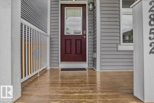 Front entry featuring a paneled door with an upper glass insert, exterior siding, a porch light fixture, and numerical house identification - 2852 Duke Crescent, Edmonton, AB 