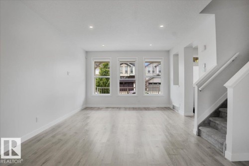 Spacious interior featuring light wood-finish flooring, recessed lighting, and three large windows - 2852 Duke Crescent, Edmonton, AB 