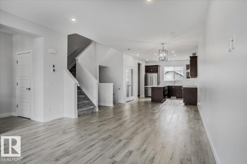 Open-concept living space featuring light wood-finish flooring, a modern kitchen with dark cabinetry, stainless steel appliances, and a central island - 2852 Duke Crescent, Edmonton, AB 