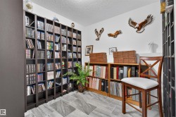 Room featuring extensive dark wood-finish built-in shelving, lighter wood-finish open shelving, white walls, and a textured ceiling - 