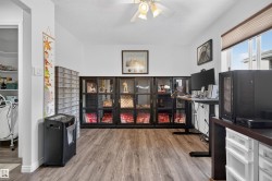 Spacious room featuring wood-finish flooring, white walls, and a ceiling fan with integrated lighting - 
