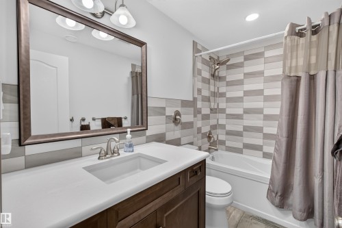 Bathroom featuring a white rectangular undermount sink set in a solid surface countertop, wood-finish vanity cabinetry, a wall-mounted mirror, and a tub/shower combination with a tiled surround - 5006 53 Avenue, Cold Lake, AB 