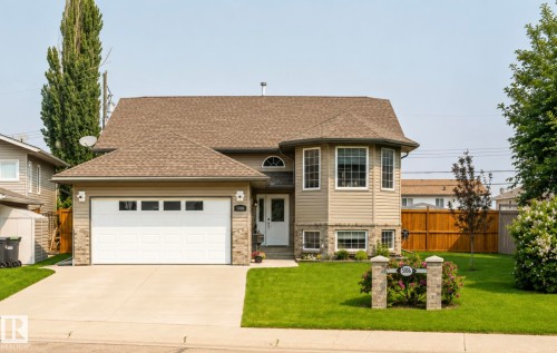 Two-story residence featuring a bay window, asphalt shingle roof, attached garage with panel windows, stone veneer accents, and a concrete driveway - 5006 53 Avenue, Cold Lake, AB 