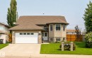 Two-story residence featuring a bay window, asphalt shingle roof, attached garage with panel windows, stone veneer accents, and a concrete driveway - 5006 53 Avenue, Cold Lake, AB 
