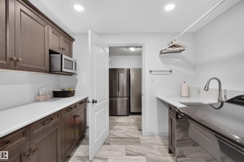 Spacious utility room featuring extensive dark wood cabinetry, white countertops, an undermount sink with a gooseneck faucet, and light-toned tile flooring - 5006 53 Avenue, Cold Lake, AB 