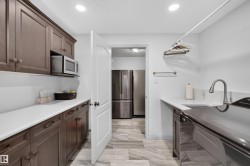 Spacious utility room featuring extensive dark wood cabinetry, white countertops, an undermount sink with a gooseneck faucet, and light-toned tile flooring - 