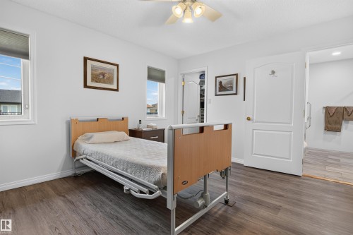 Spacious room featuring wood-finish flooring, two windows with blinds, a ceiling fan with integrated lighting, and a white paneled door - 5006 53 Avenue, Cold Lake, AB 