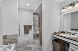 Bathroom featuring a walk-in shower with tiled walls and grab bars, a separate bathtub, a single vanity with an oval sink and countertop, and recessed ceiling lighting - 