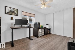 Bright interior space featuring wood-finish flooring, a window with horizontal blinds, a ceiling fan with integrated lighting, and multiple sliding closet doors - 