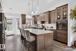 Spacious kitchen featuring a large central island with seating, extensive dark wood cabinetry, stainless steel appliances, and wood-finish flooring - 