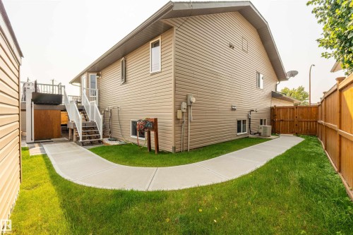Exterior featuring tan siding, a curved concrete pathway, a wooden privacy fence, and a multi-level deck with white railings - 5006 53 Avenue, Cold Lake, AB 