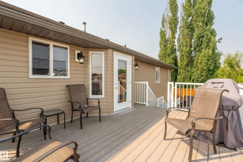 Multi-level composite deck featuring white railings, a brown vinyl-sided exterior, and mature trees providing a natural backdrop - 5006 53 Avenue, Cold Lake, AB 