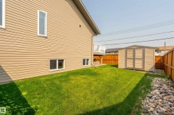 Expansive grassy yard featuring a beige storage shed, perimeter wood fencing, and a decorative rock border - 