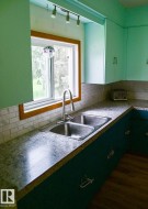 Kitchen area featuring a double basin stainless steel sink with a gooseneck faucet, light-toned countertops, and a white subway tile backsplash - 