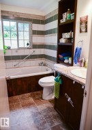 Bathroom featuring a built-in tub, tiled shower surround, recessed shelving, and vanity with an integrated sink - 
