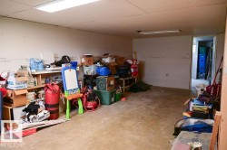 Unfinished basement space featuring exposed drywall, concrete flooring, and fluorescent lighting fixtures - 