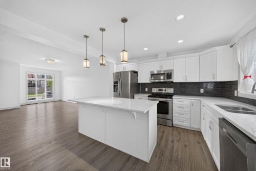 Contemporary kitchen featuring a center island with a stone countertop, stainless steel appliances, white cabinetry, and dark tile backsplash - 227 Cy Becker Blvd, Edmonton, AB 