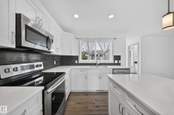 Modern kitchen featuring white cabinetry, stainless steel appliances, dark tile backsplash, a center island, and wood-finish flooring - 