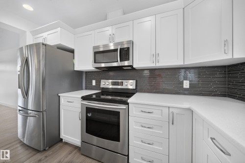 Contemporary kitchen featuring white cabinetry, stainless steel appliances, light countertops, and a dark mosaic tile backsplash - 227 Cy Becker Blvd, Edmonton, AB 