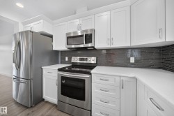 Contemporary kitchen featuring white cabinetry, stainless steel appliances, light countertops, and a dark mosaic tile backsplash - 