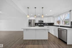 Contemporary kitchen featuring an island with pendant lighting, white cabinetry, dark subway tile backsplash, stainless steel appliances, and wood-finish flooring - 