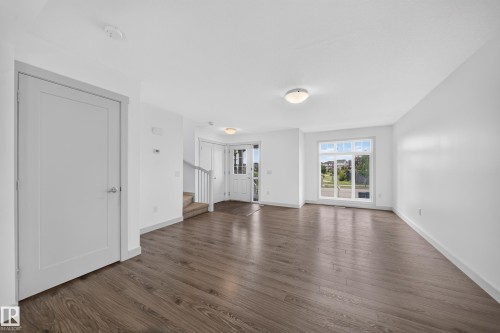 Spacious open-concept living area featuring wood-finish flooring, abundant natural light from large windows, white walls, and contemporary doors - 227 Cy Becker Blvd, Edmonton, AB 