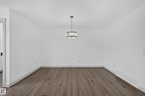Spacious room with wood-finish flooring and a contemporary drum pendant light fixture - 227 Cy Becker Blvd, Edmonton, AB 
