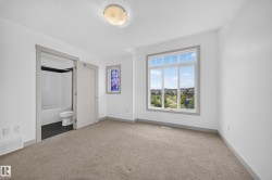 Carpeted room featuring a large window with white framing, a stained-glass accent window, and an en-suite bathroom with dark floor tiling and a white tub/shower combination - 