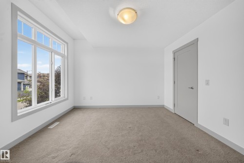 Room featuring a large multi-pane window, neutral-toned carpeting, white walls, and a flush mount ceiling light - 227 Cy Becker Blvd, Edmonton, AB 