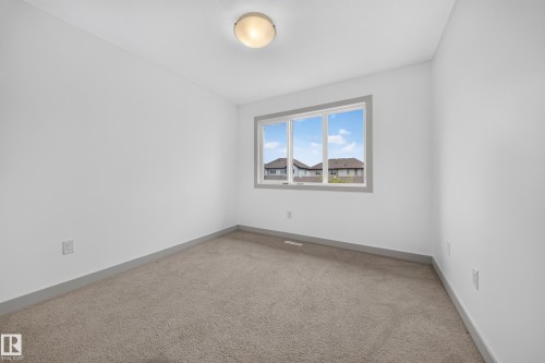 Bright room featuring neutral carpeting, white walls, and a window with grey trim - 227 Cy Becker Blvd, Edmonton, AB 