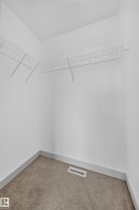 Walk-in closet featuring built-in wire shelving, plush carpeting, white baseboards, and a floor vent - 
