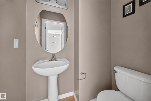 Pedestal sink with chrome faucet, an oval wall-mounted mirror, and a two-bulb vanity light fixture - 227 Cy Becker Blvd, Edmonton, AB 
