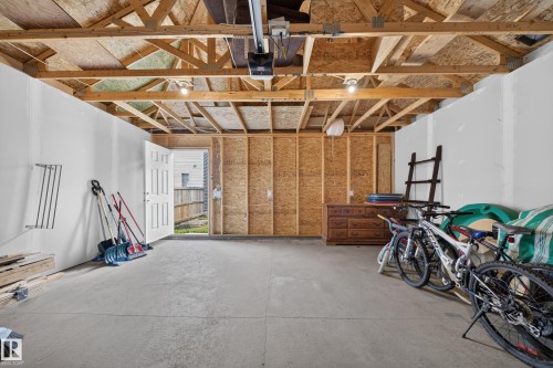 Unfinished garage space featuring exposed wood trusses, concrete flooring, and a side access door - 227 Cy Becker Blvd, Edmonton, AB 