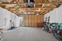 Unfinished garage space featuring exposed wood trusses, concrete flooring, and a side access door - 