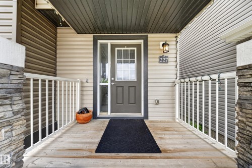 Inviting front entryway featuring a wooden porch, white railings, and stacked stone pillar accents - 227 Cy Becker Blvd, Edmonton, AB 
