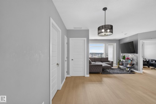 Open-concept living area featuring wood-finish flooring, a modern drum pendant light fixture, and light gray wall tones - 706 5151 Windermere Boulevard, Edmonton, AB 