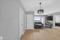 Open-concept living area featuring wood-finish flooring, a modern drum pendant light fixture, and light gray wall tones - 