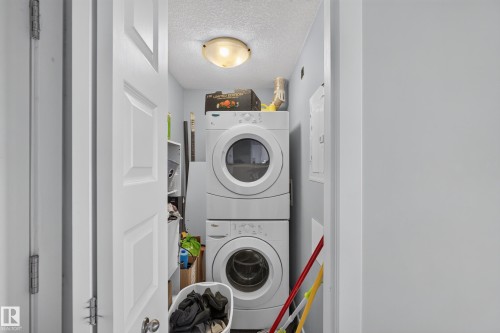 Dedicated laundry area featuring a stacked washer and dryer unit, overhead flush-mount lighting, and light blue wall paint - 706 5151 Windermere Boulevard, Edmonton, AB 