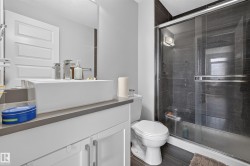Bathroom featuring a glass-enclosed shower with dark tile surround, a vessel sink on a vanity with white cabinetry, and wood-finish flooring - 