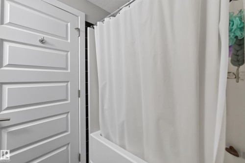 White paneled interior door with chrome hardware, featuring a full bathtub with a shower curtain - 706 5151 Windermere Boulevard, Edmonton, AB 