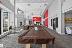Spacious common area featuring high ceilings, contemporary pendant lighting, extensive window lines, a built-in fireplace, and patterned carpet flooring - 
