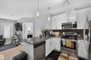 Modern kitchen featuring white cabinetry, stainless steel appliances, a dark tile backsplash, and light wood-finish flooring - 706 5151 Windermere Boulevard, Edmonton, AB 