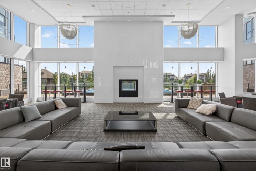 Spacious communal room featuring a floor-to-ceiling window wall, a central fireplace, recessed lighting, and modern pendant light fixtures - 706 5151 Windermere Boulevard, Edmonton, AB 