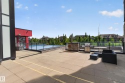 Outdoor paved patio area featuring a stone-clad built-in barbecue station, glass railing, and a visible swimming pool - 